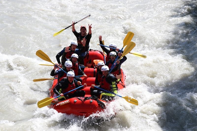 Personen in einem Schlauchboot mit Helmen und Paddeln auf einem wilden Fluss.