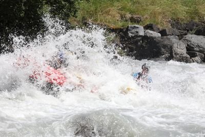 People in inflatable boats with helmets and life jackets in the whitewater river, surrounded by rocks.