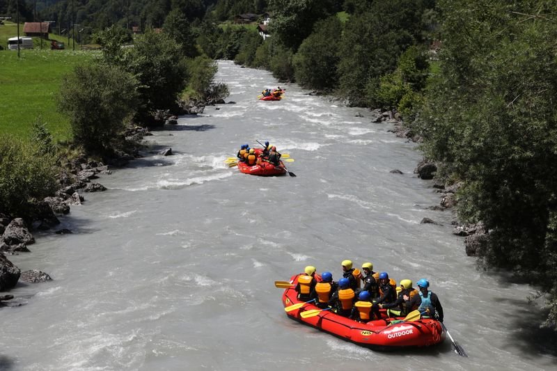 People in inflatable boats with helmets and life jackets on a river in a mountainous landscape.