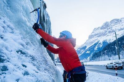 Ein Mann hängt an einem Eispickel mit roter Jacke in Grindelwald, Schweiz.