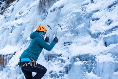 Das Mädchen übt Eisklettern mit zwei Eispickeln.