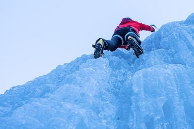 Die Person klettert an einem gefrorenen Wasserfall hoch und erreicht die Spitze.