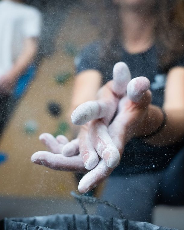 Climber applying chalk to hands in an indoor climbing gym, blurred wall holds in background.