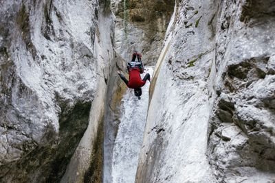 Person in rotem Neoprenanzug und Helm seilt sich in einer engen Schlucht mit einem Wasserfall ab.
