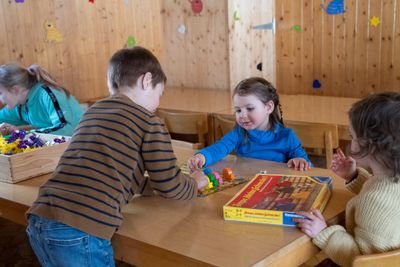 Children are playing with building blocks at a wooden table in a room with wooden walls.
