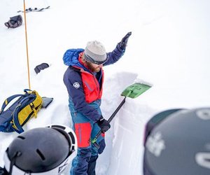 Bergführer zeigt Lawinenkurs Teilnehmenden Schneeaufbau mit Lawinenschaufel