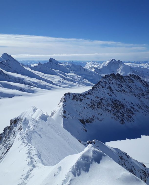 Snow-covered mountain peaks under a clear blue sky in a vast alpine landscape.