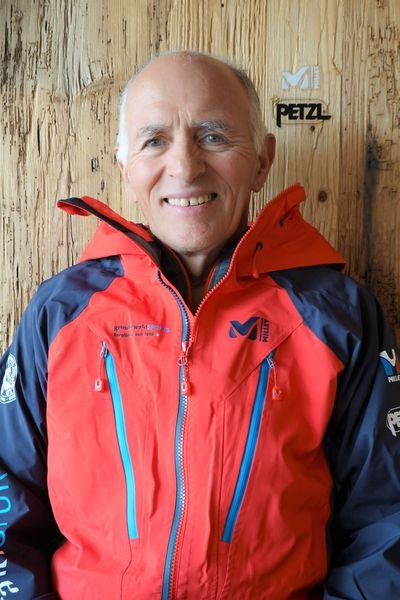 Mann in einer Millet Gortex Jacke vor einem holzigen Hintergrund