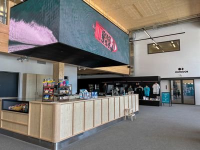 Reception area with wooden counter, digital screen above, and merchandise on display.