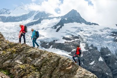 A group of mountain climbers is walking along a ridge. In the background, the glacier-covered mountain landscape can be seen.