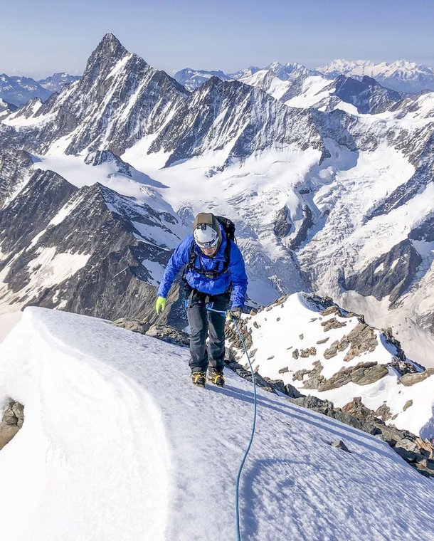 Climber ascends snowy mountain ridge, surrounded by peaks.