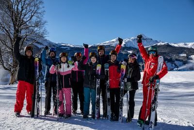 Gruppe von Skifahrern in Helmen und Skibrillen, die Skier an einem verschneiten Berghang mit klarem Himmel halten.
