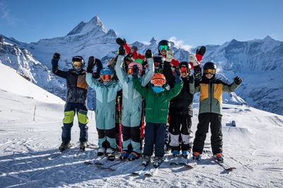 Group of skiers with helmets and ski goggles on a snow-covered mountain in front of an alpine backdrop.