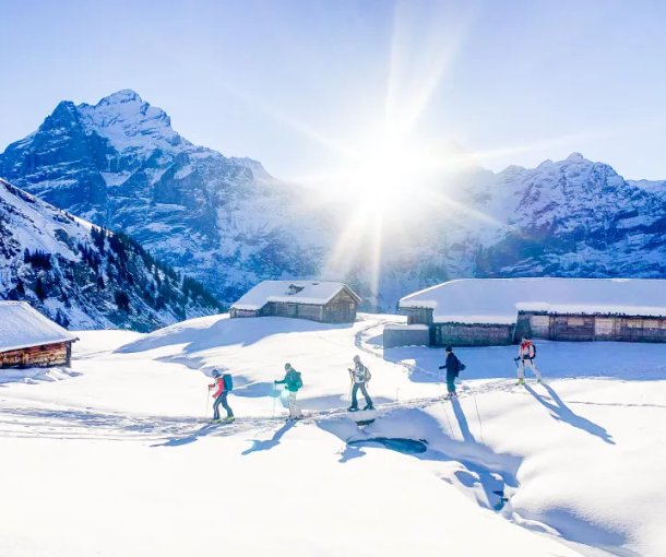 Ski tourers ascending near alpine huts with the Wetterhorn in the background.