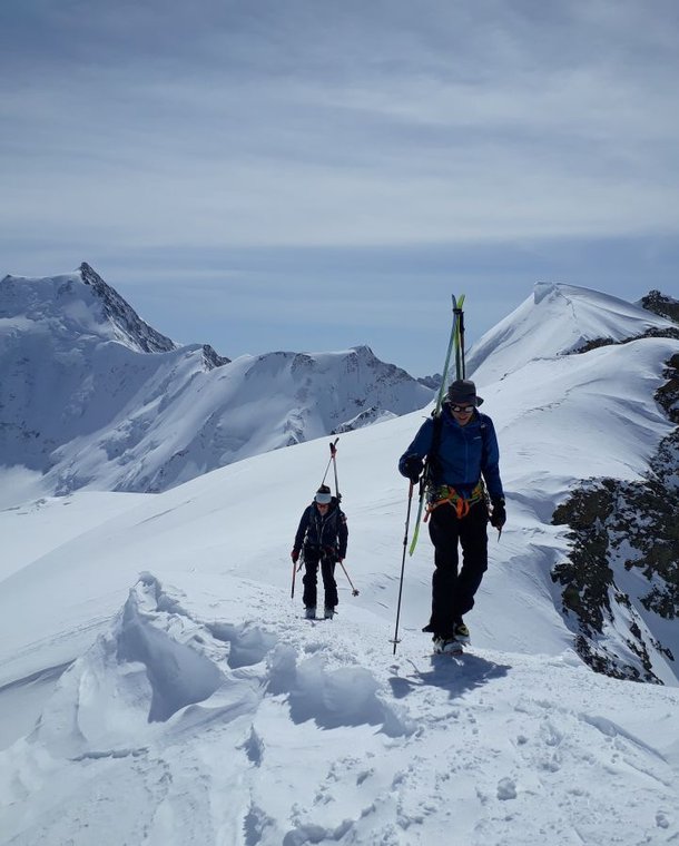Ski tourers with skis strapped on their backs on a ridge.
