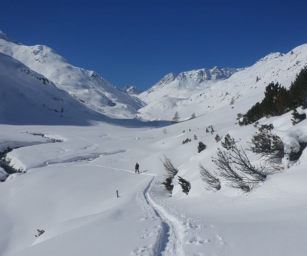 Ski tourers ascending through a snow-covered valley with a stream.