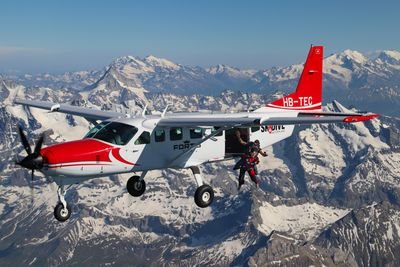 Parachutist with helmet and suit jumps out of airplane over snow-covered Alps.