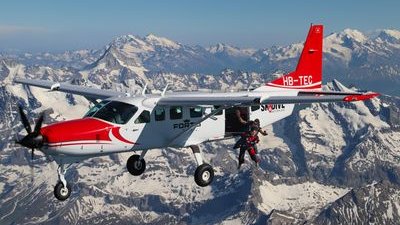 Parachutist with helmet and suit jumps out of airplane over snow-covered Alps.