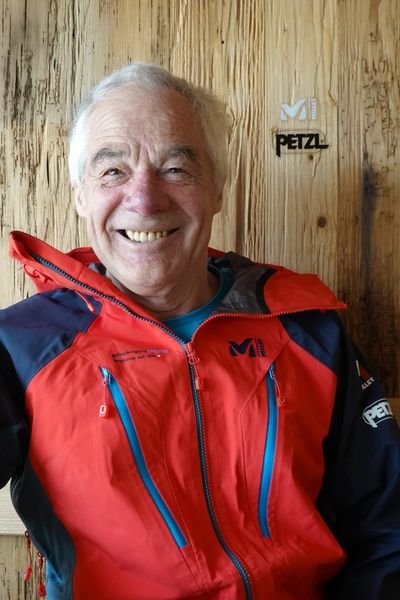 Ein man in einem roten Millet Jacke is smiling at the camera.