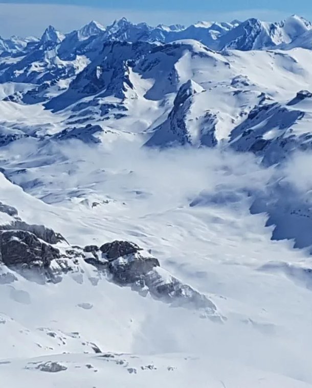 Snow-covered mountain range with peaks and valleys under a clear blue sky.