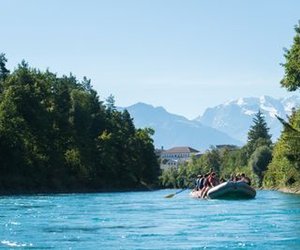 Schlauchtboot treibt auf der Aare zwischen Thun und Bern, umgeben von Bäumen, Berge im Hintergrund