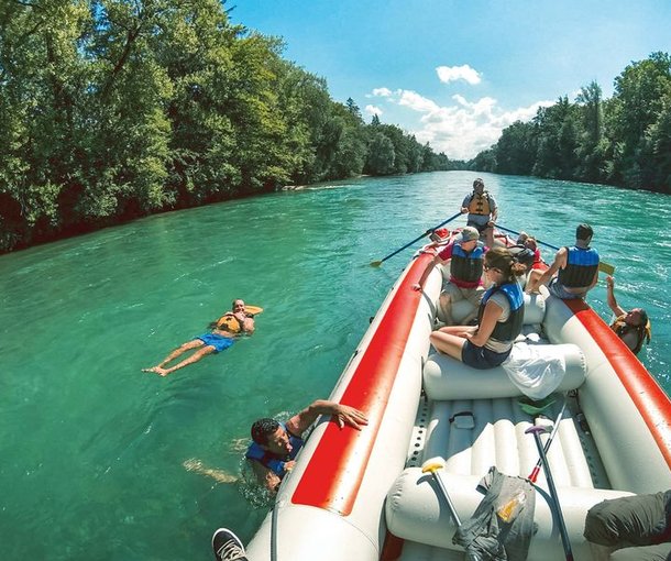 Menschen auf einem Raft während der Aare Flussfahrt, einige Teilnehmer lassen sich neben den Boot treiben