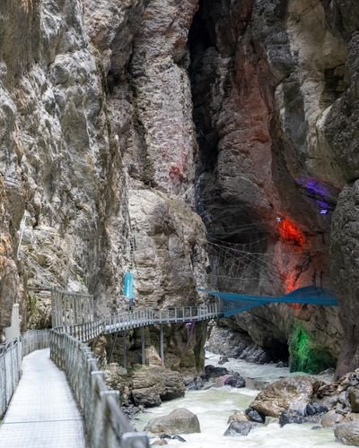 Metal walkway and suspension bridge with safety nets, ladders and rigging inside a steep rocky canyon above a rushing river.
