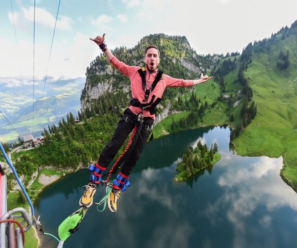 Person bungee jumping over a lake, wearing a safety harness, mountains in the background.