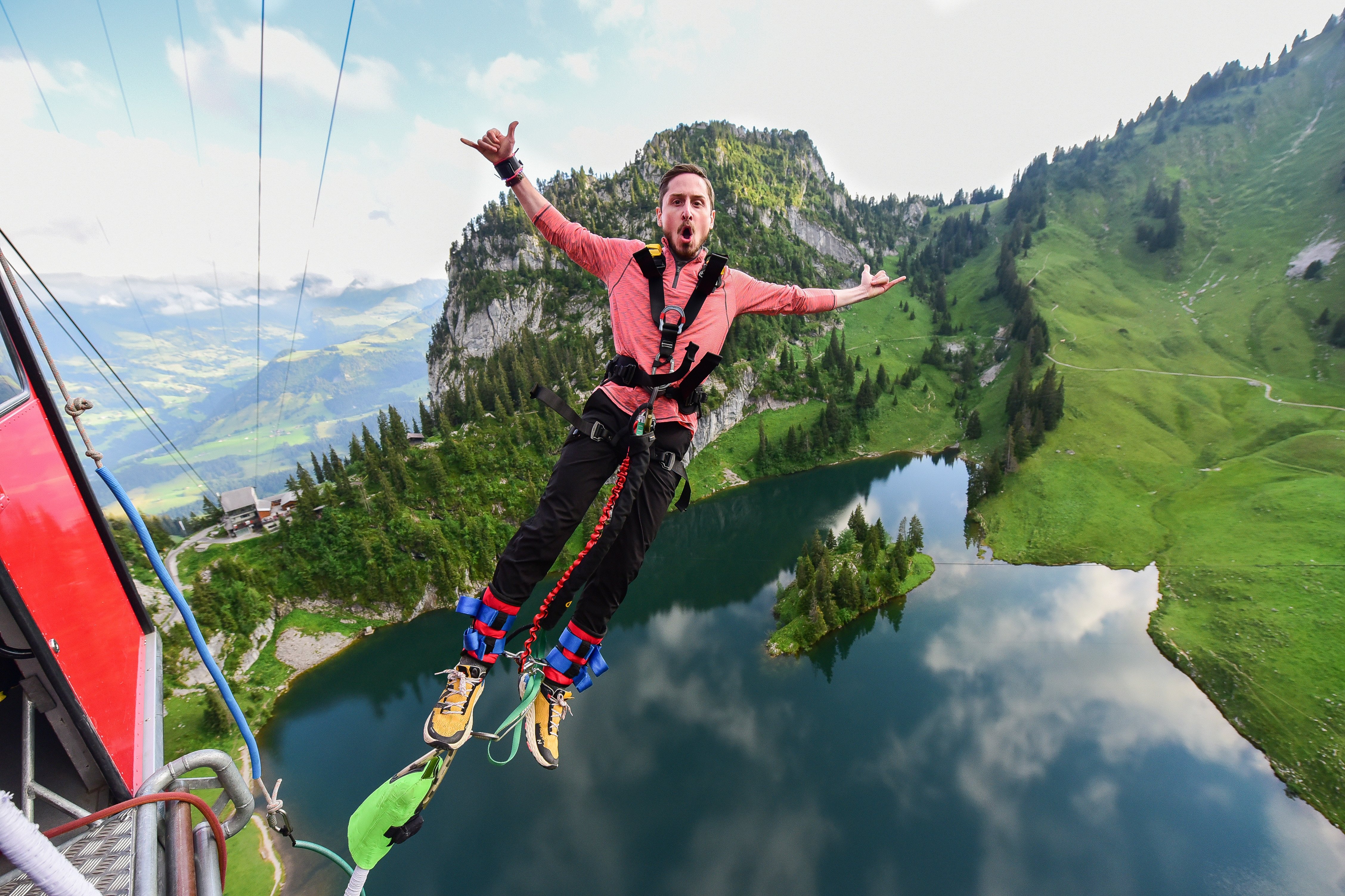 Person bungee jumping over a lake, wearing a safety harness, mountains in the background.