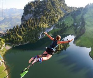 Person bungee jumping over a mountain lake at sunset with arms outstretched wide