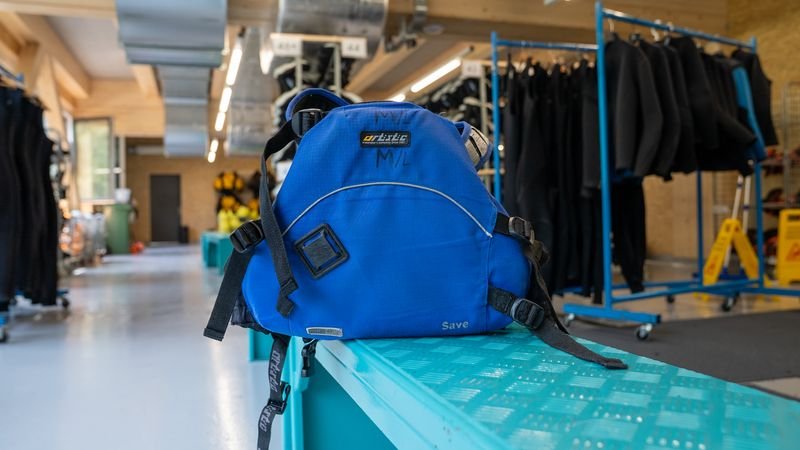 Blue climbing harness with straps and buckles is lying on a blue shelf in a room with climbing equipment.