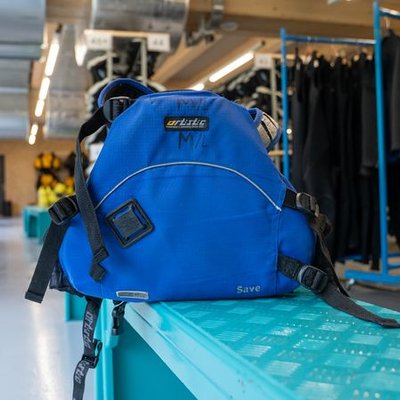Blue climbing harness with straps and buckles is lying on a blue shelf in a room with climbing equipment.
