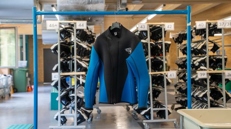 Neoprene suit in blue and black hangs on a blue metal rack in a room with shelves full of more suits.