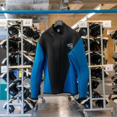 Neoprene suit in blue and black hangs on a blue metal rack in a room with shelves full of more suits.