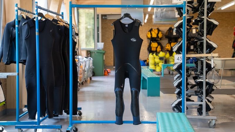 Wetsuits are hanging in a rental room with other equipment for water sports.
