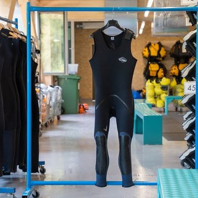 Wetsuits are hanging in a rental room with other equipment for water sports.