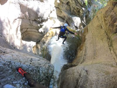 Person in Helm und Neoprenanzug springt in einen Canyon-Wasserfall, mit sichtbaren Felswänden und fließendem Wasser.