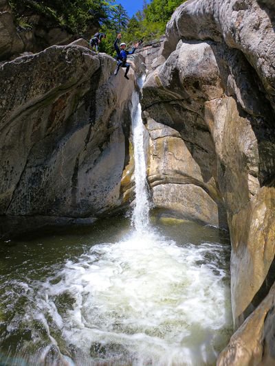 Person in Helm und Neoprenanzug springt in den Canyon-Pool; der Guide beobachtet von oben.