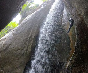 Person rappelling beside a waterfall in a canyon, wearing a helmet and harness.