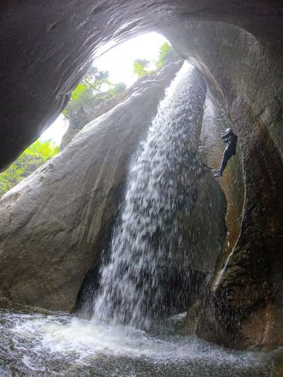 Person, der neben einem Wasserfall in einer Schlucht abseilt, trägt einen Helm und ein Gurtzeug.
