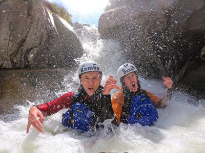 Zwei Personen beim Canyoning in einem felsigen Wasserlauf, die Helme und Rettungswesten tragen, spritzen im Wasser herum.