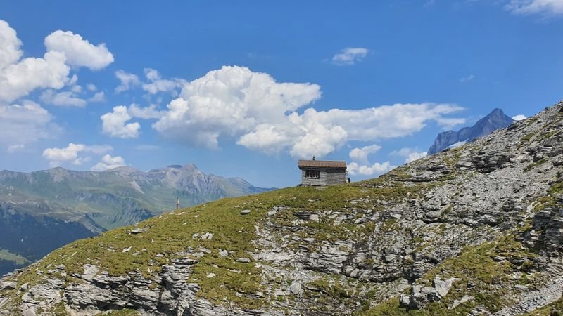 Small mountain hut on a grassy rocky ridge under a blue sky.