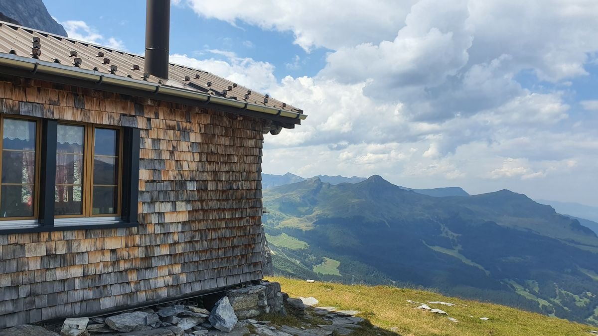 Mountain hut beside alpine slopes under a cloudy sky.