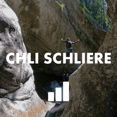 Person mit Helm und Klettergurt springt in einen felsigen Canyon-Pool mit anderen unten im Sonnenlicht.