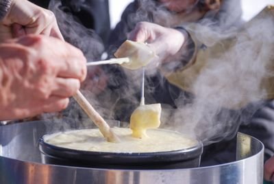 Personen tauchen Brot in einen Topf mit geschmolzenem Käse, im Freien bei kühlem Wetter.