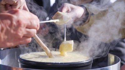 Personen tauchen Brot in einen Topf mit geschmolzenem Käse, im Freien bei kühlem Wetter.