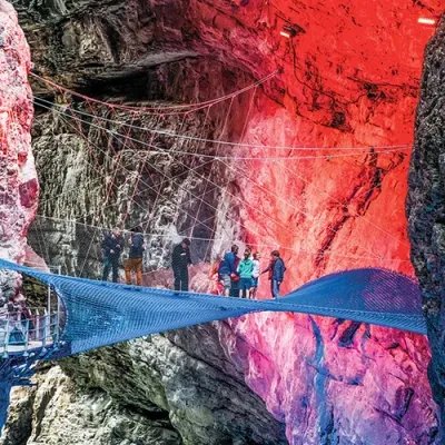People on a tense net in an illuminated gorge, surrounded by rock walls.