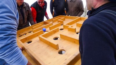 Personen balancieren einen Holztisch mit einem Labyrinth und einer blauen Kugel.