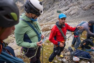 Gruppe von Kletterern, die Helme und Gurte tragen und Seile in felsigem Gebirgsterrain handhaben.