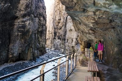 People on a bridge in a gorge, surrounded by rocks and a flowing stream.